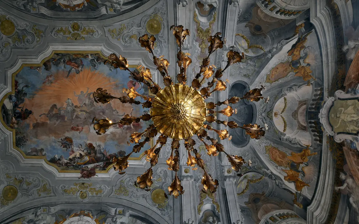 A gilded chandelier beneath a painted ballroom ceiling