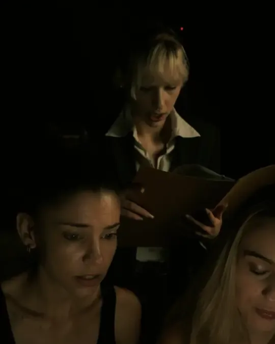 An agent reads from a dossier to two players in a dark room