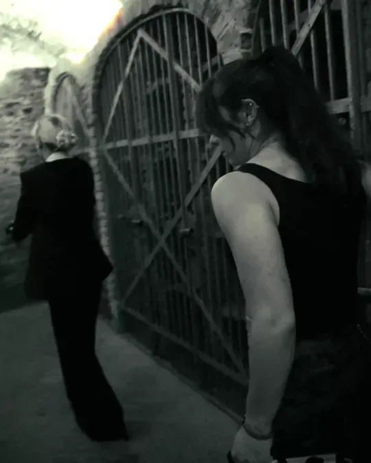 Two women walk past an iron gate in a vaulted cellar
