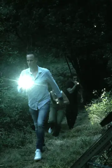 Three people moving through a dark wood at night, lit by a torch